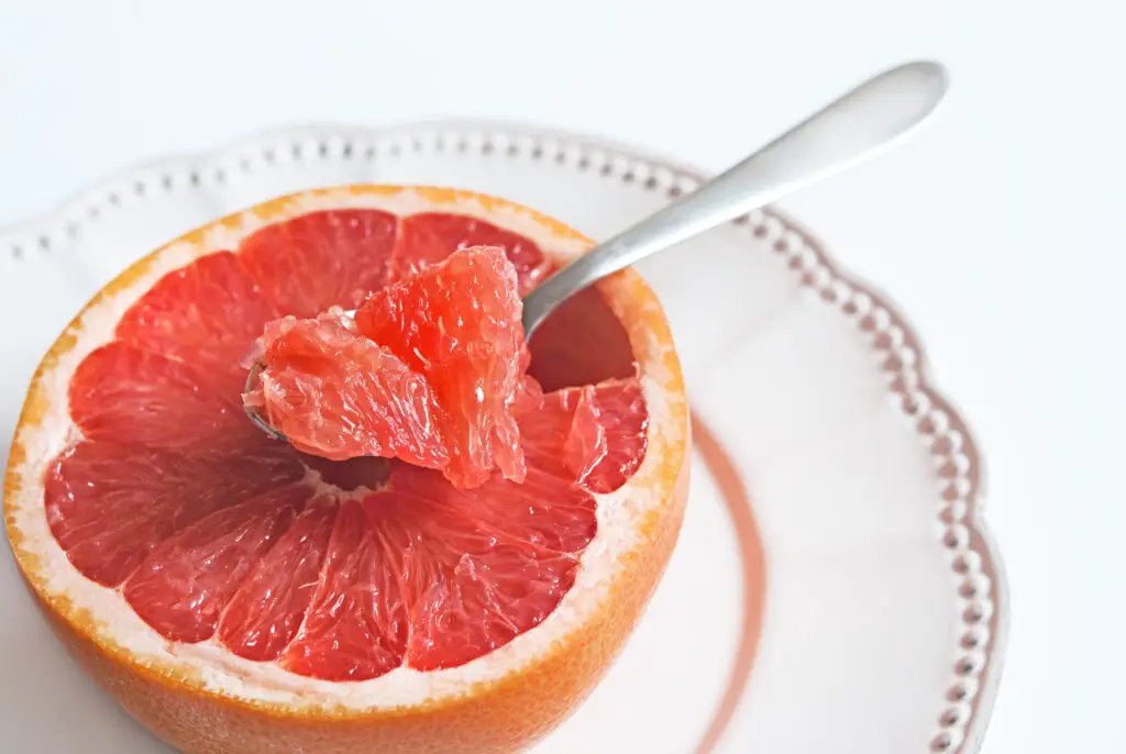 Piece of pink grapefruit in a tea-spoon, healthy citrus dessert