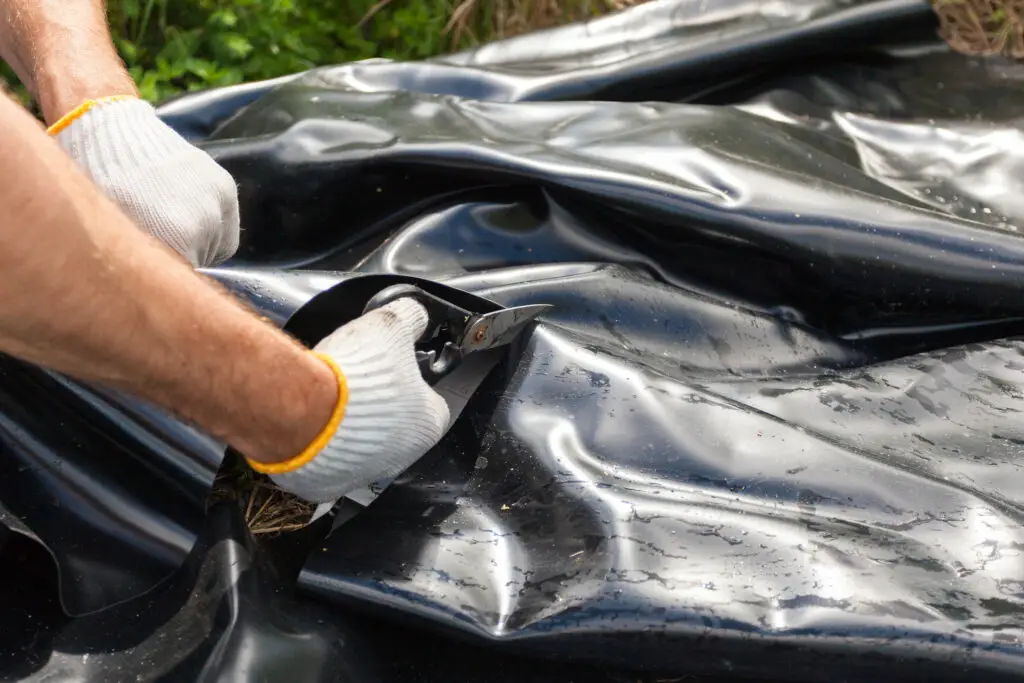 Worker in white gloves put a black vinyl sheet cover hole on the ground to be used as a pond for fish